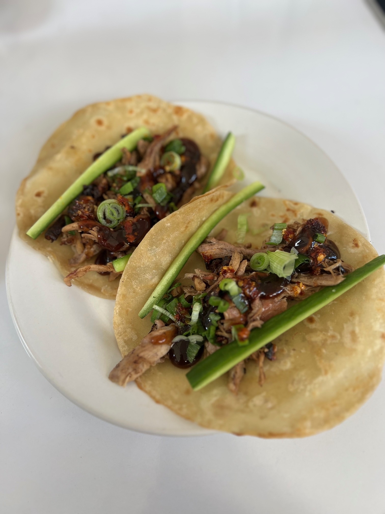 Two tacos with shredded meat and green onions on a white plate