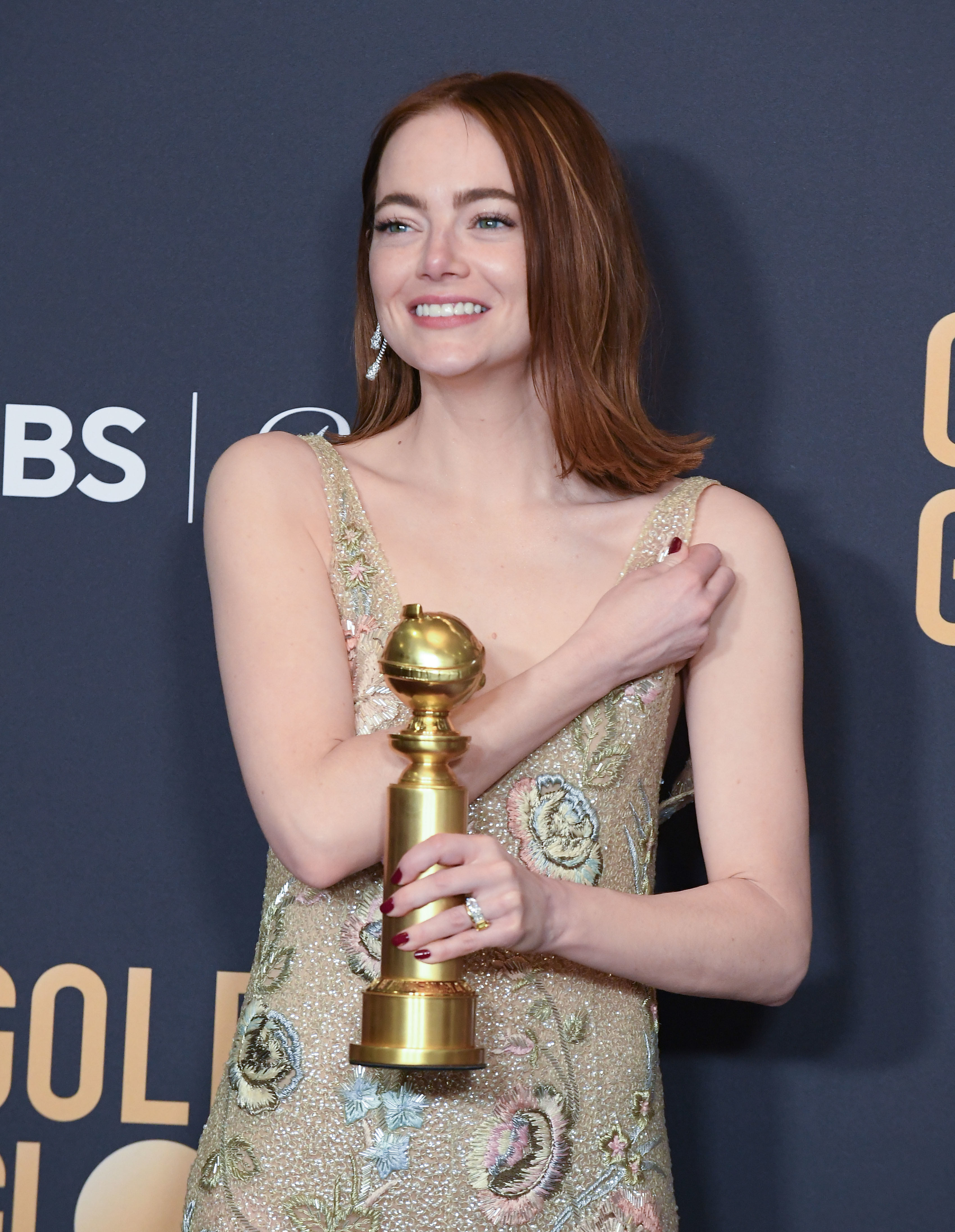 Emma Stone wearing an embellished gown, holding a Golden Globe award, smiling