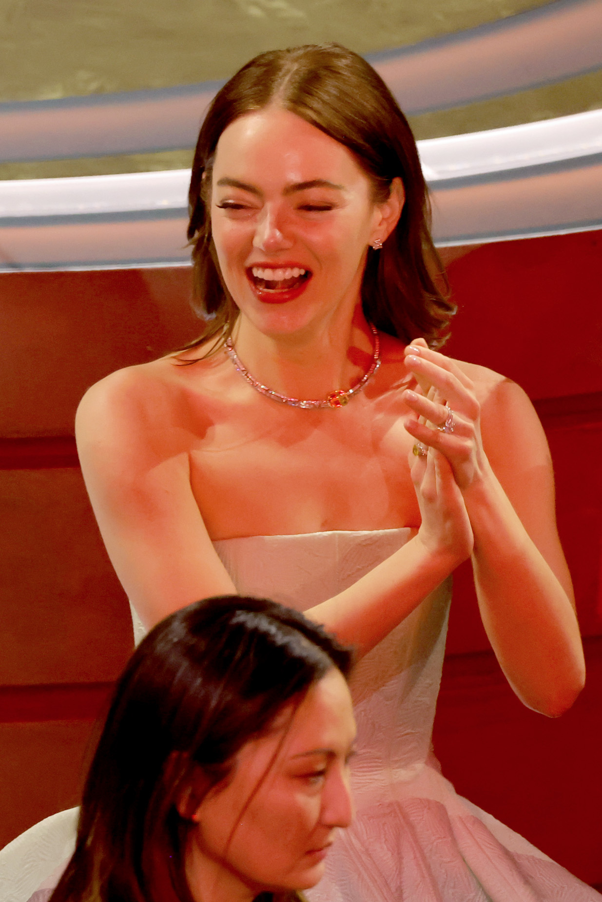 Emma Stone in a strapless gown laughing and clapping
