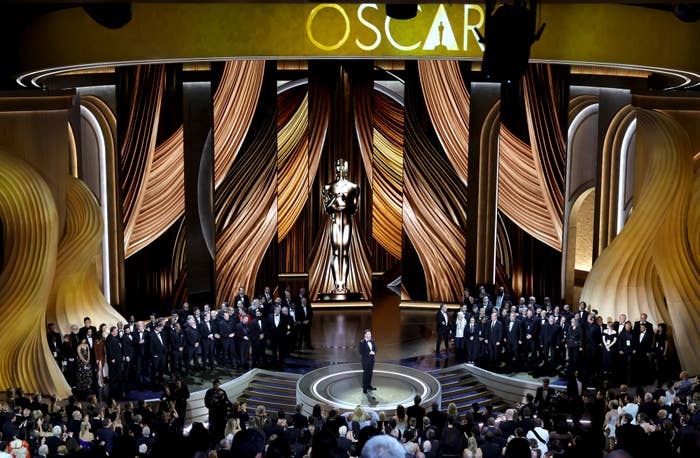 People on stage at the Oscars with a person speaking at the podium