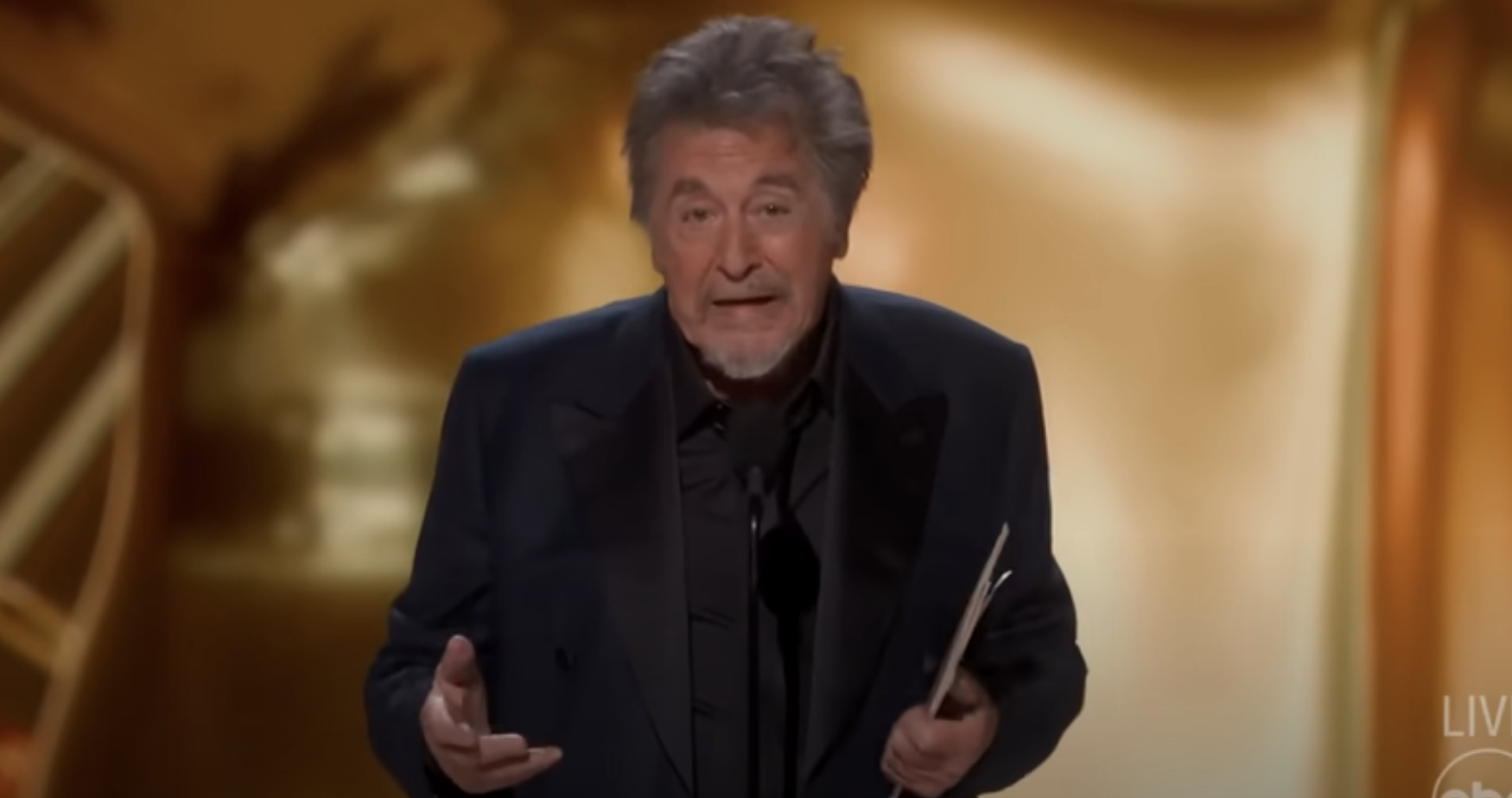 Al onstage giving a speech at an awards ceremony, holding a card