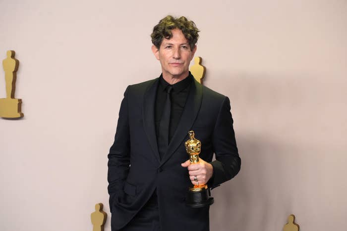 Jonathan stands with an Oscar, wearing a formal black suit and tie