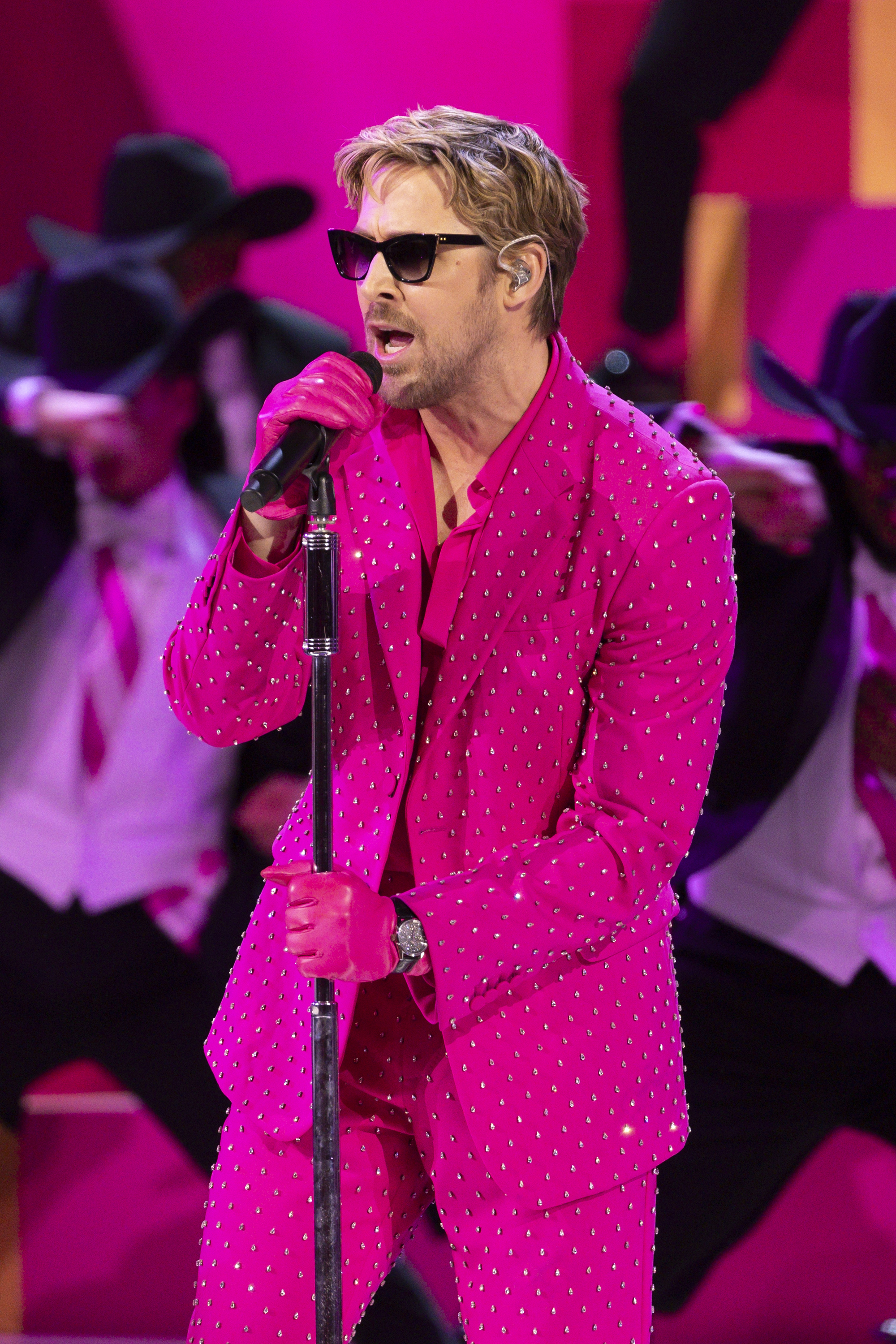 Ryan Gosling in a pink dotted suit singing into a microphone on stage