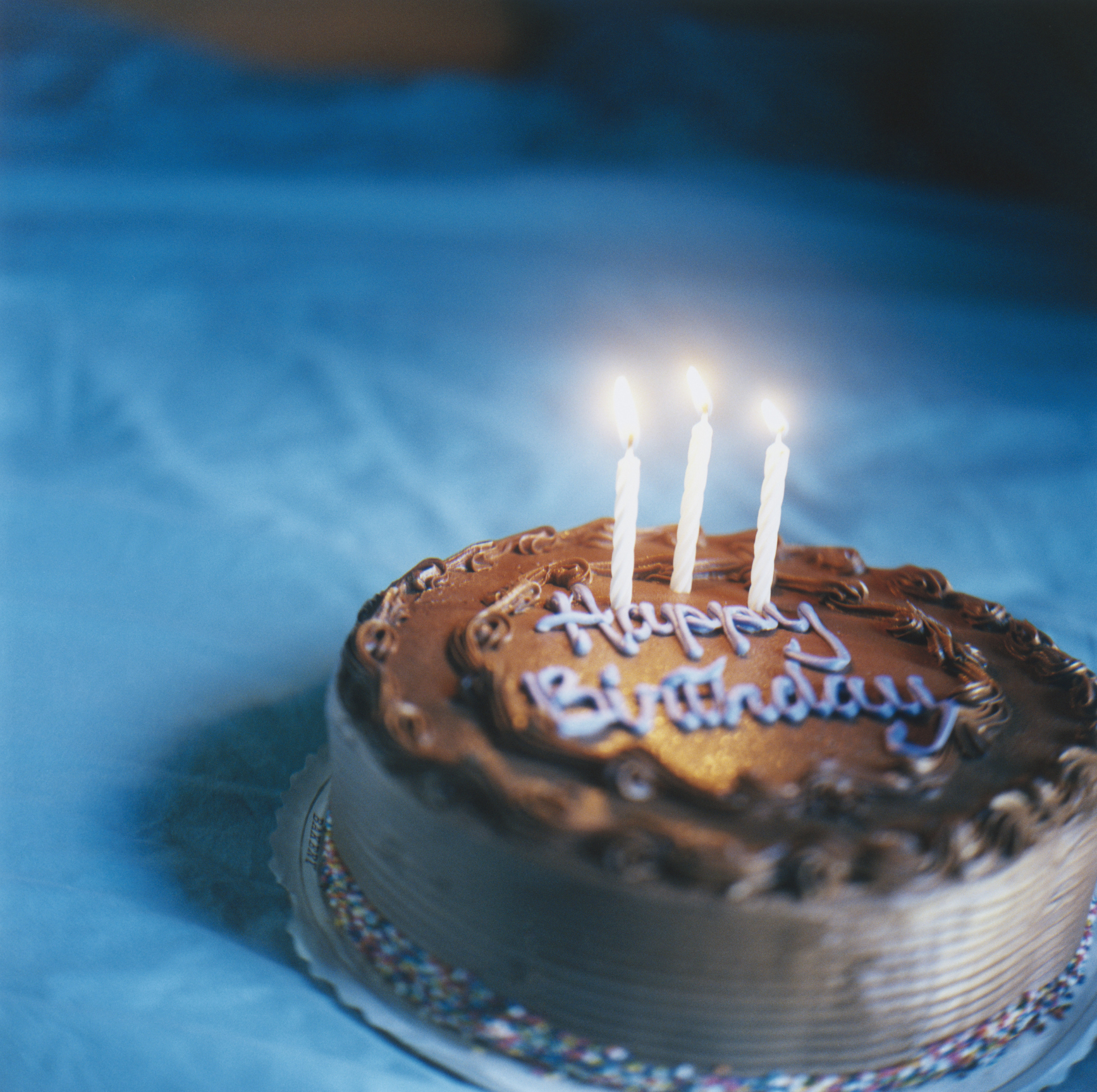 A birthday cake with lit candles and &quot;Happy Birthday&quot; icing text