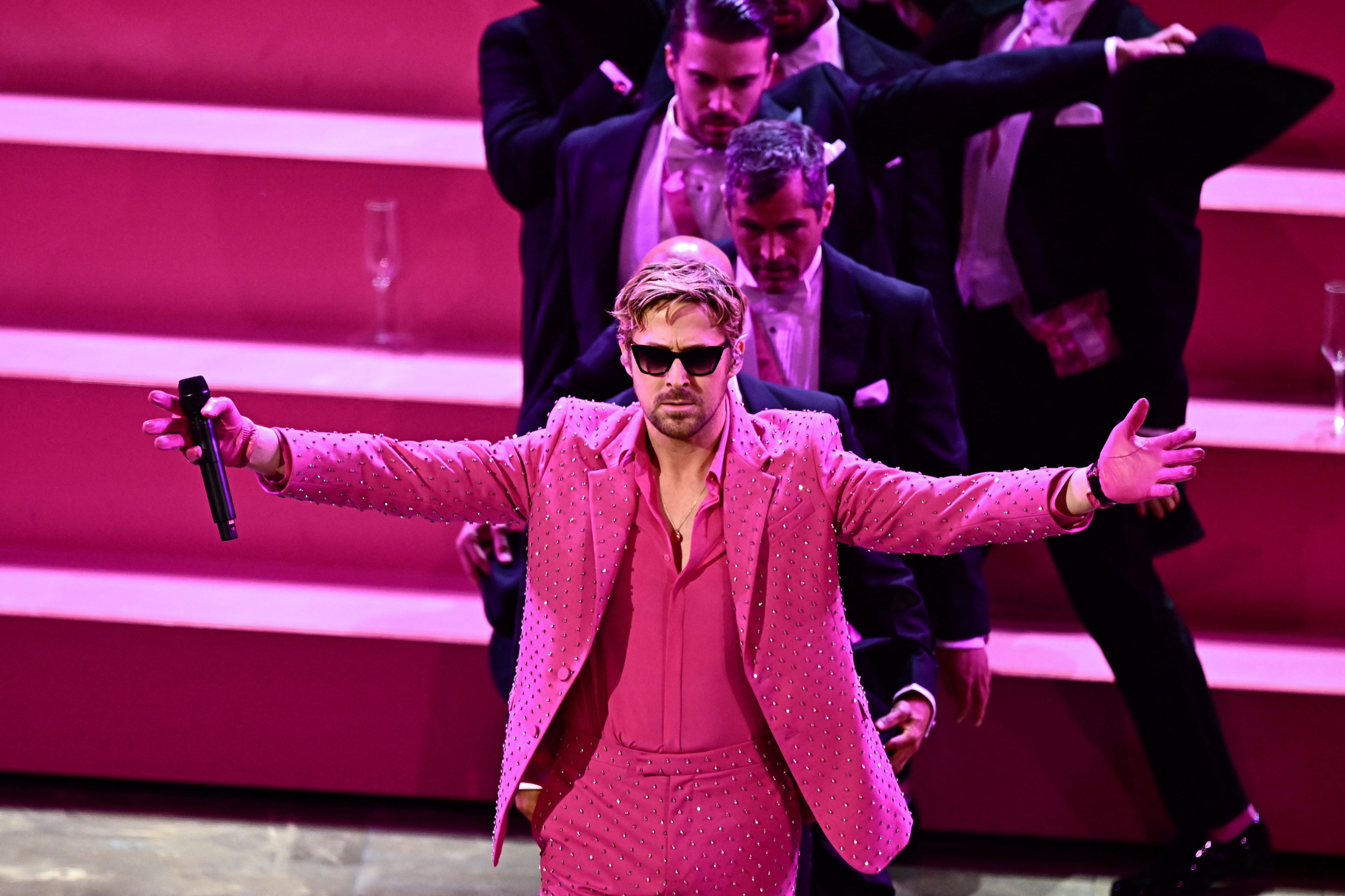 Ryan Gosling on stage in a sparkling pink jacket with arms outstretched