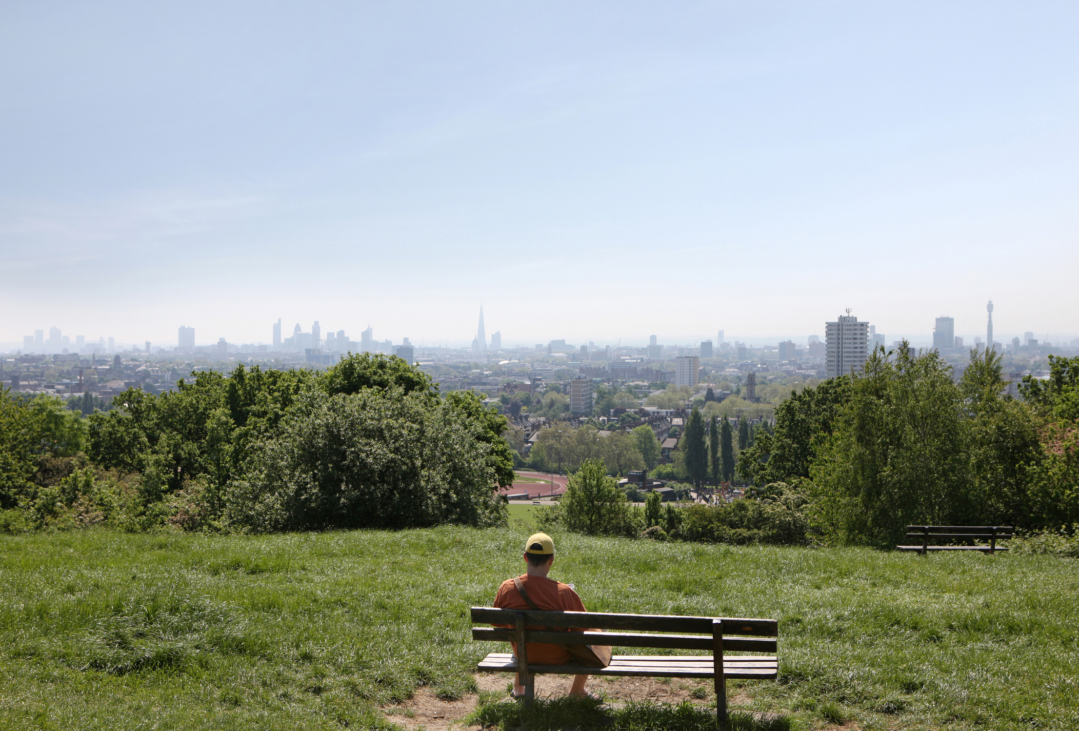 Person sitting on a park bench looking at a distant city skyline