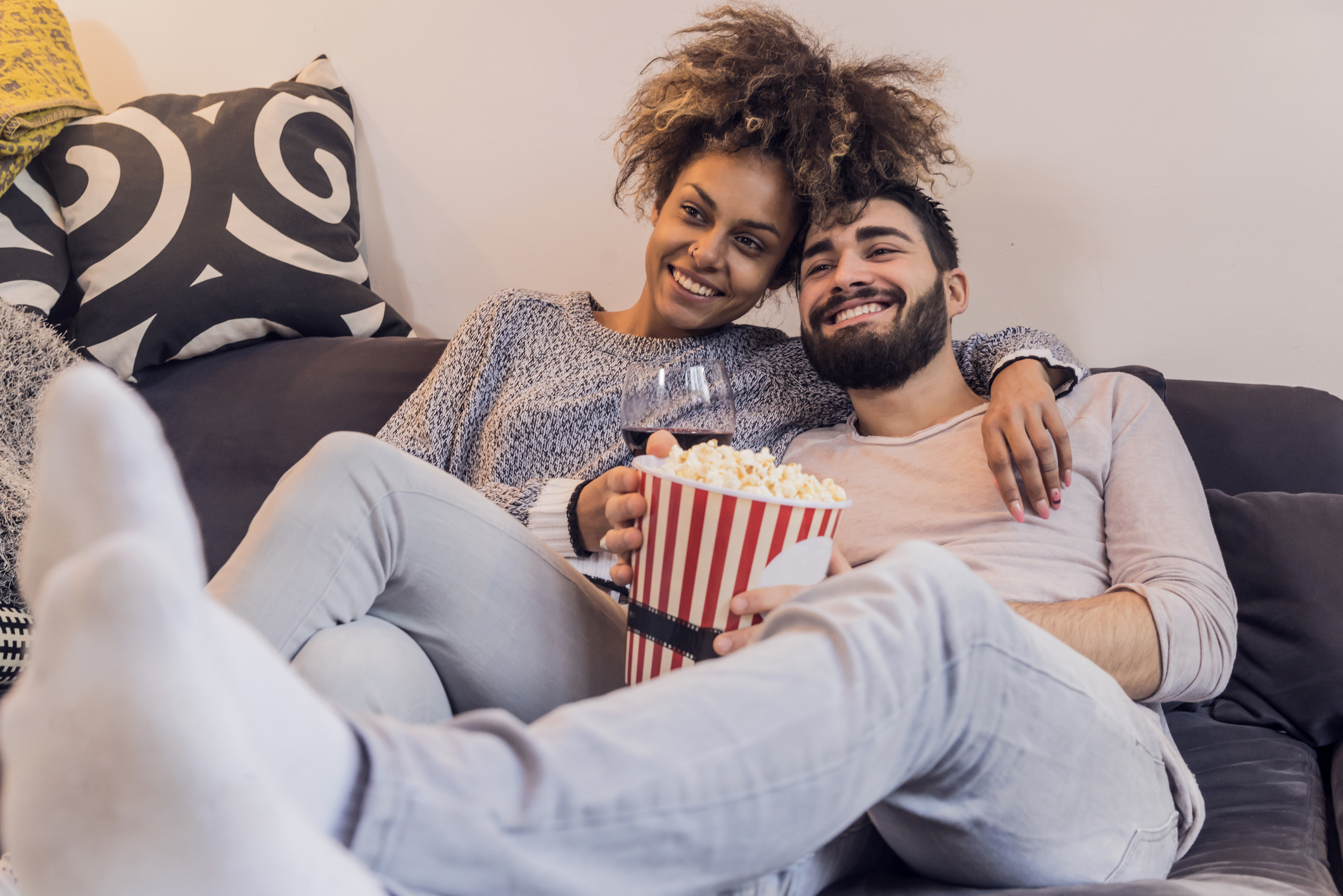 A couple sitting together on a couch sharing popcorn with a relaxed posture