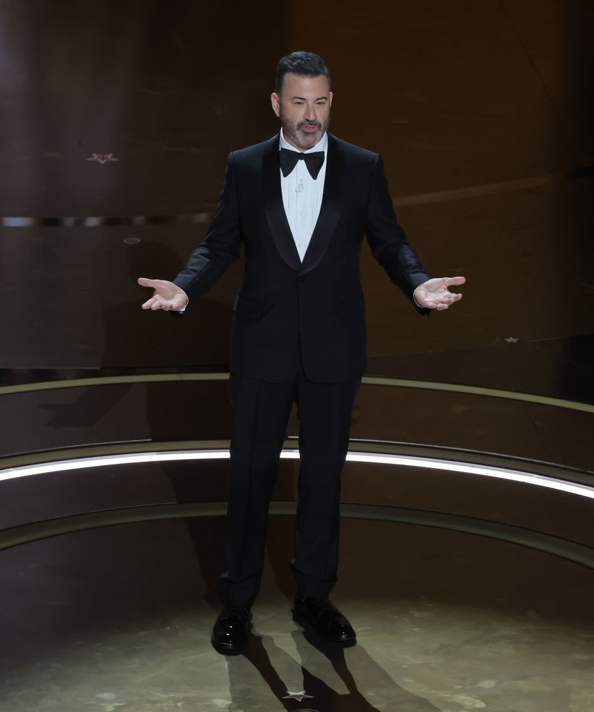 Jimmy in a tuxedo on stage with outstretched arms, hosting an event