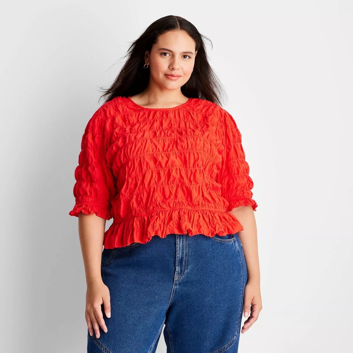 model in a textured red top and blue jeans posing for a shopping article