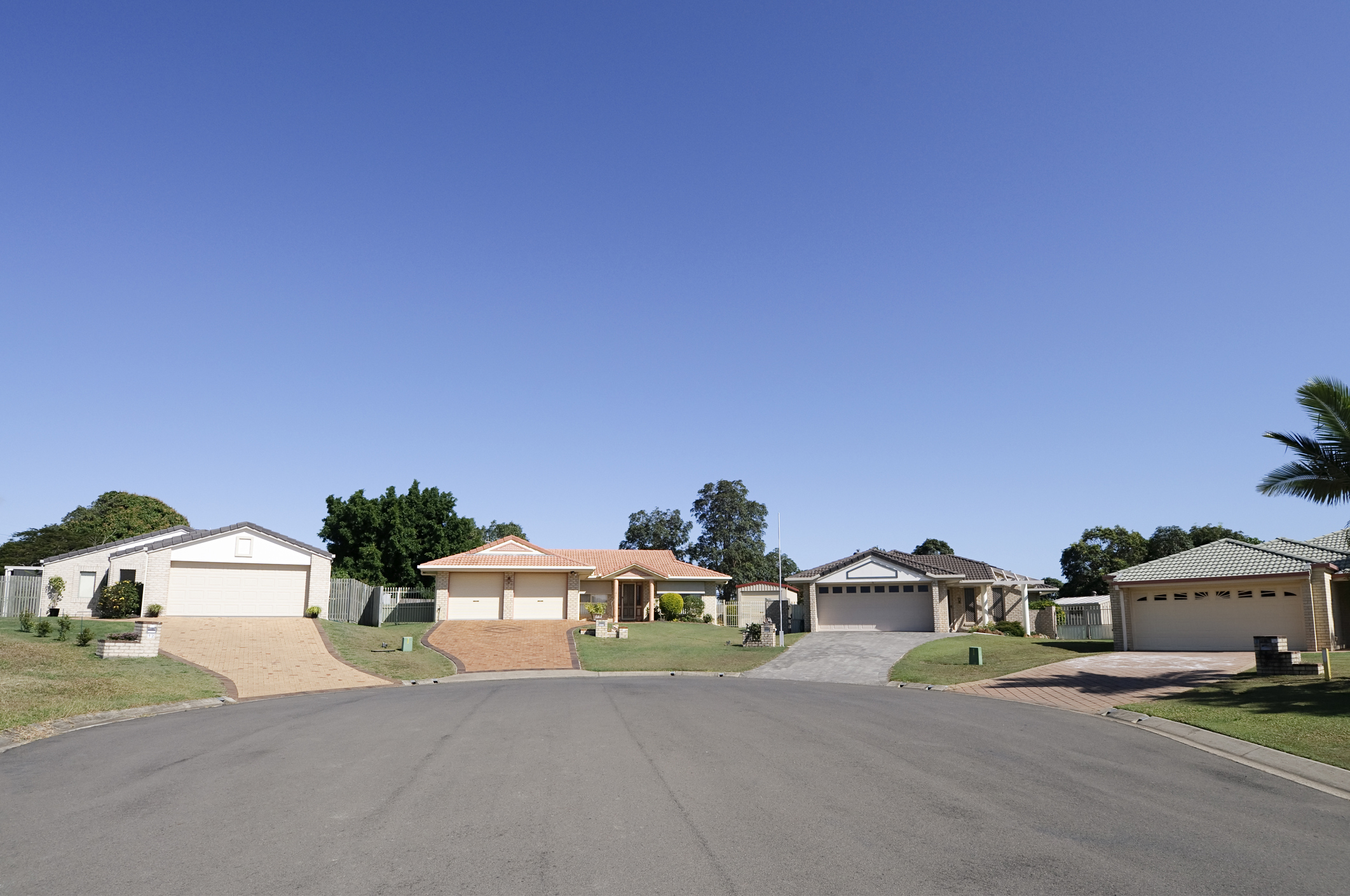 Suburban street view with four houses, driveways and manicured lawns under a clear sky