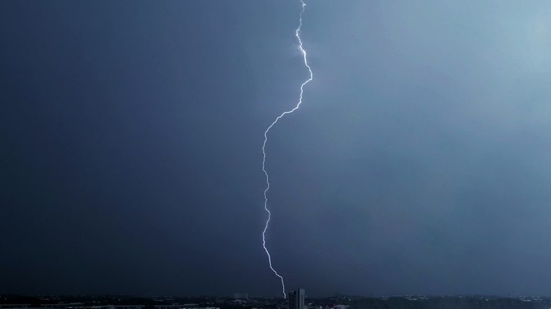 Lightning bolt striking over cityscape under stormy skies