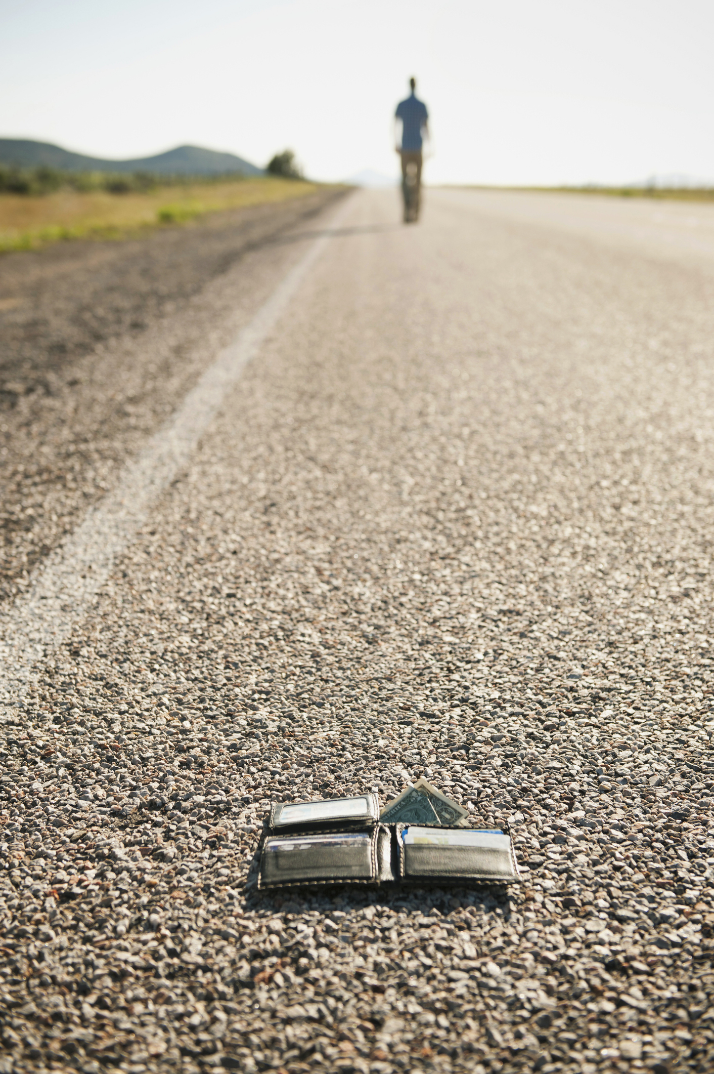 A wallet lies on a road with a blurred person walking away in the distance