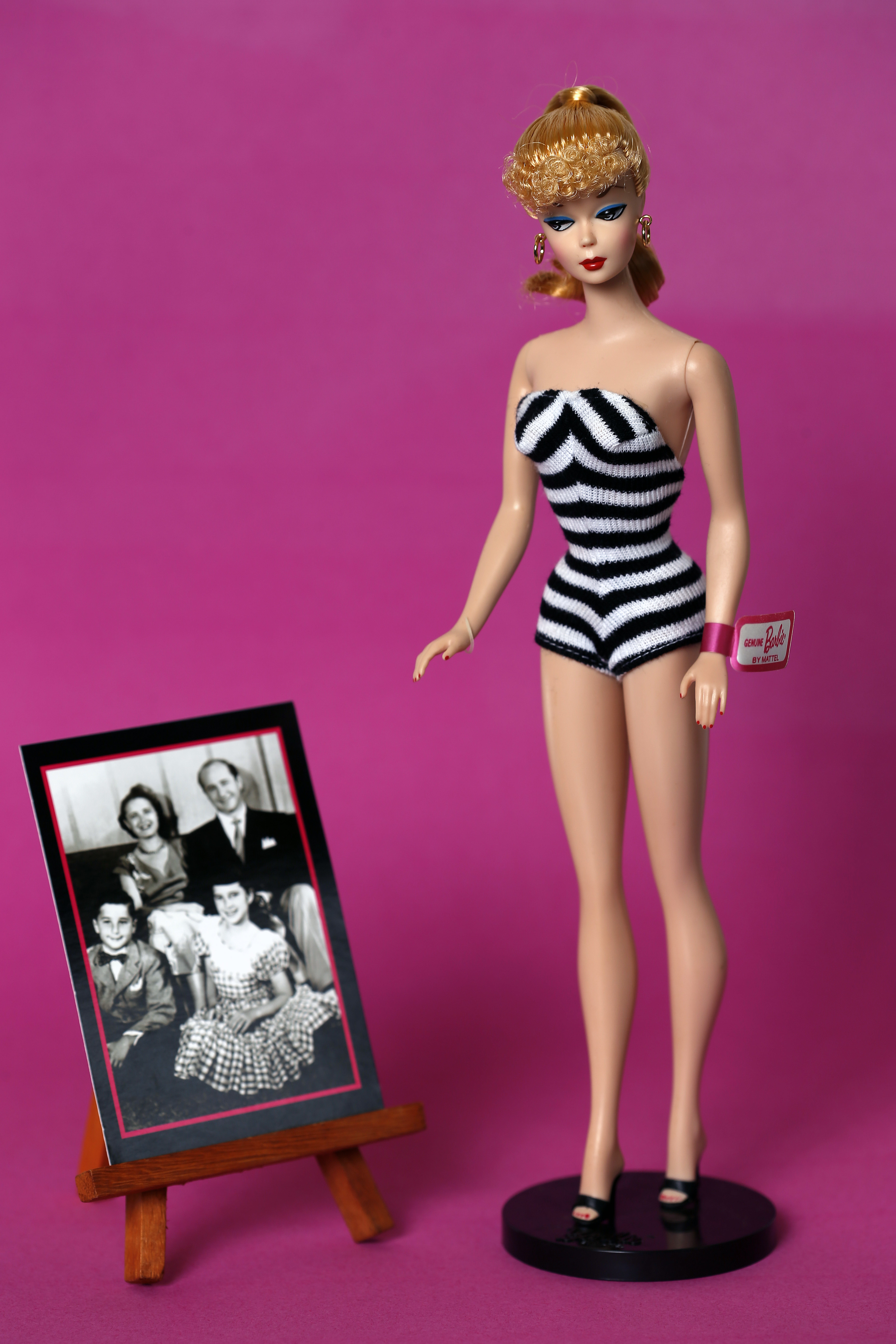 Barbie doll in vintage-style swimsuit stands next to a small easel displaying a black-and-white family photo