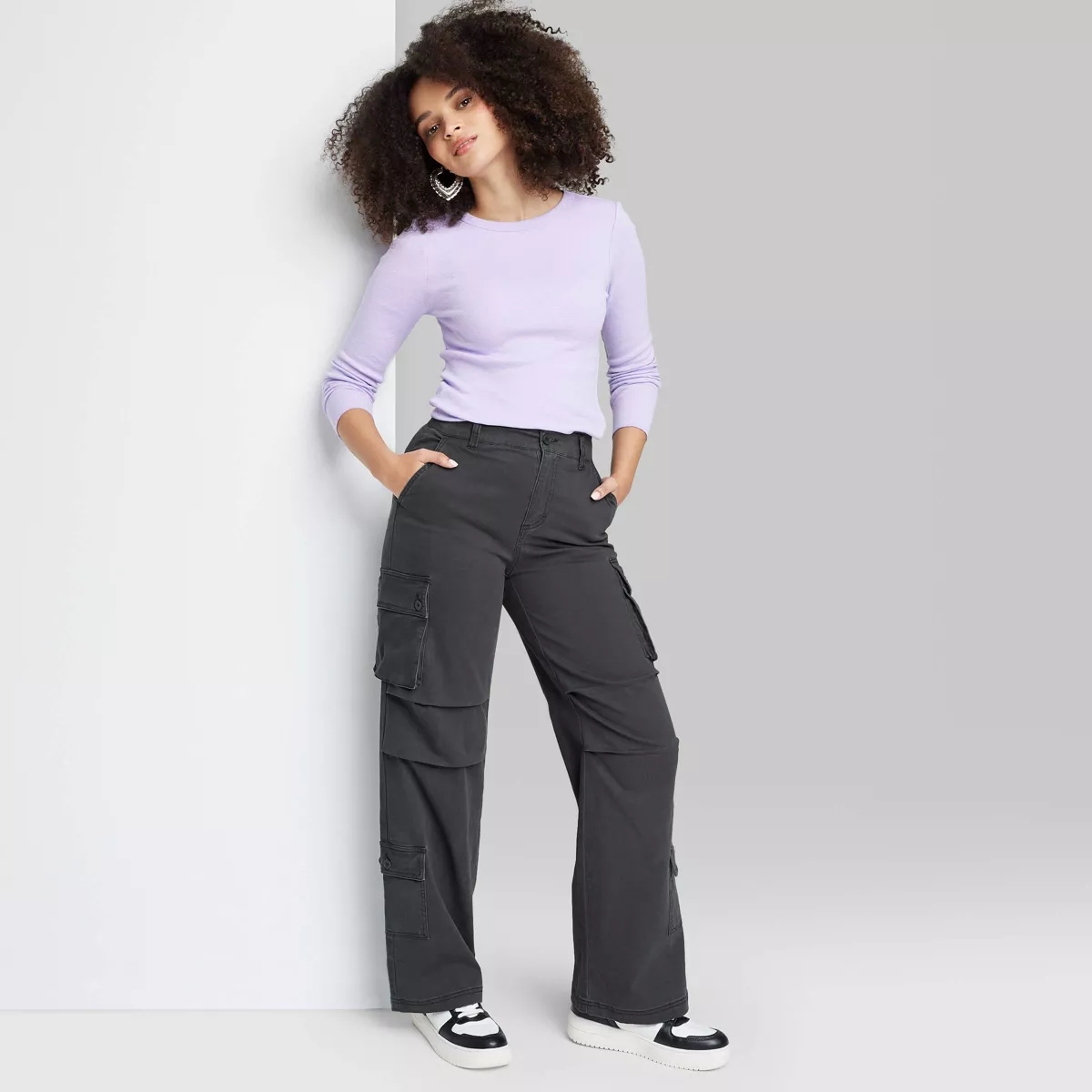 model posing in a lavender top and gray cargo pants, hand on hip, looking towards the camera