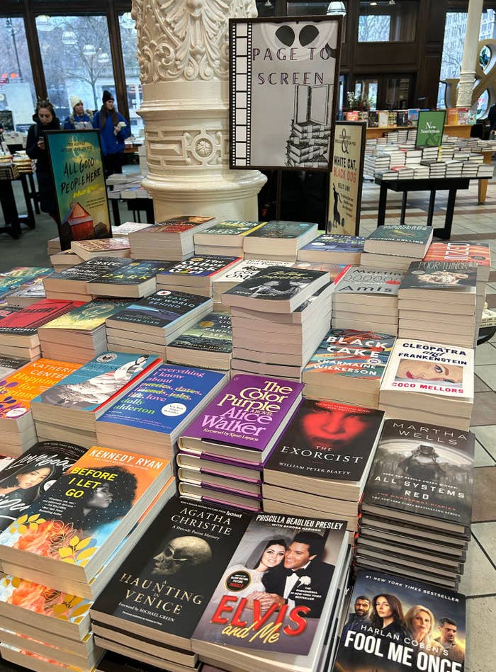 A display of various books with some titles visible, set in a bookstore with shoppers in the background