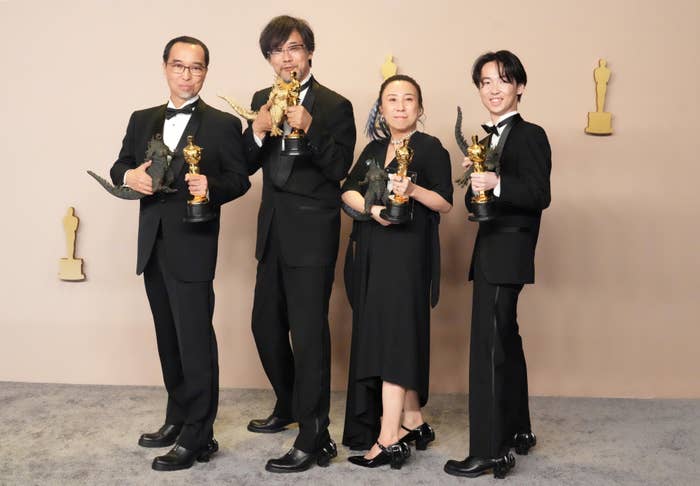 Four people in formal attire award trophies, posing for a photo