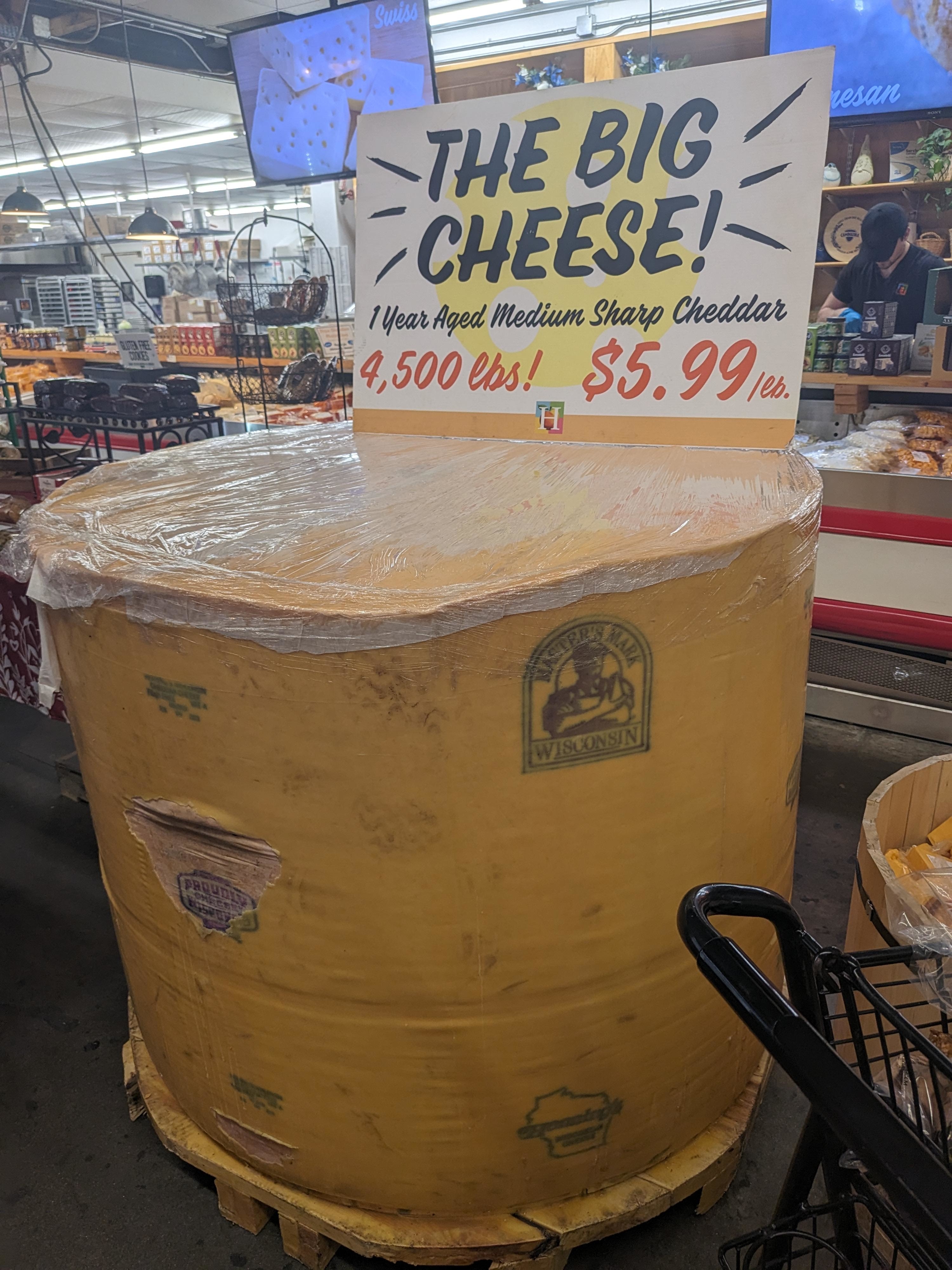 Giant wheel of cheddar cheese for sale at $5.99/lb, labeled &quot;THE BIG CHEESE,&quot; weighing 4,500 lbs