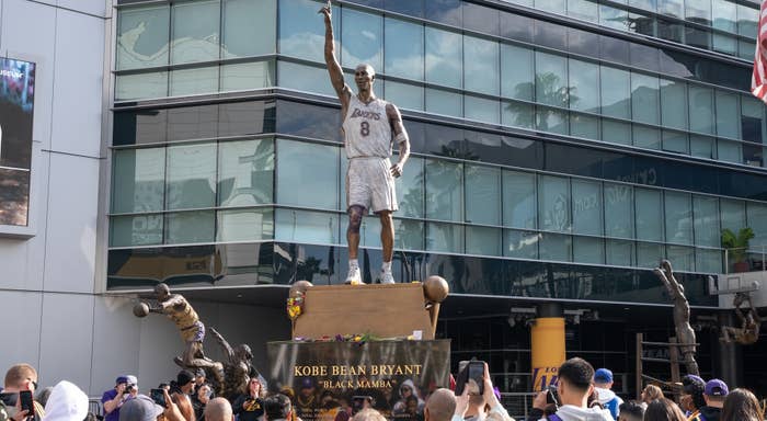 Statue of Kobe Bryant in Lakers uniform outside, with fans gathered around its base