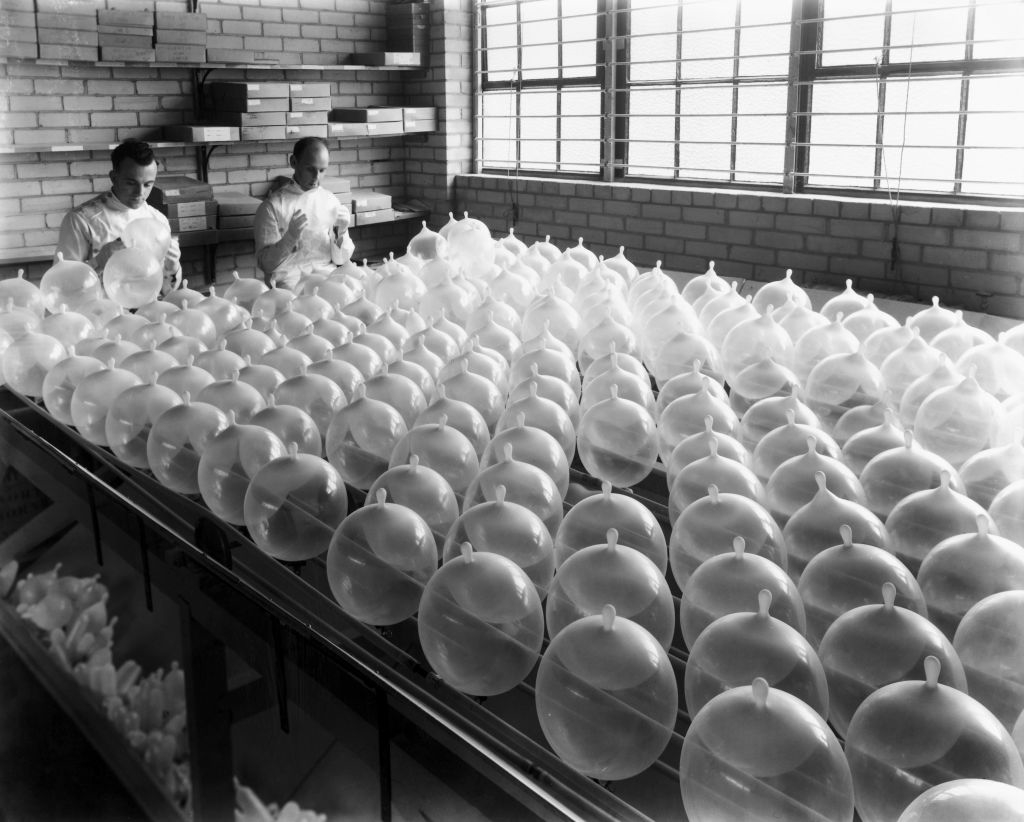 Two workers inspecting a large number of expanded condoms on a factory table