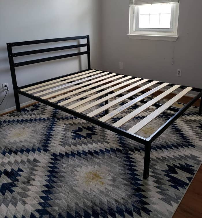 Metal bed frame with wooden slats on geometric patterned rug in a room