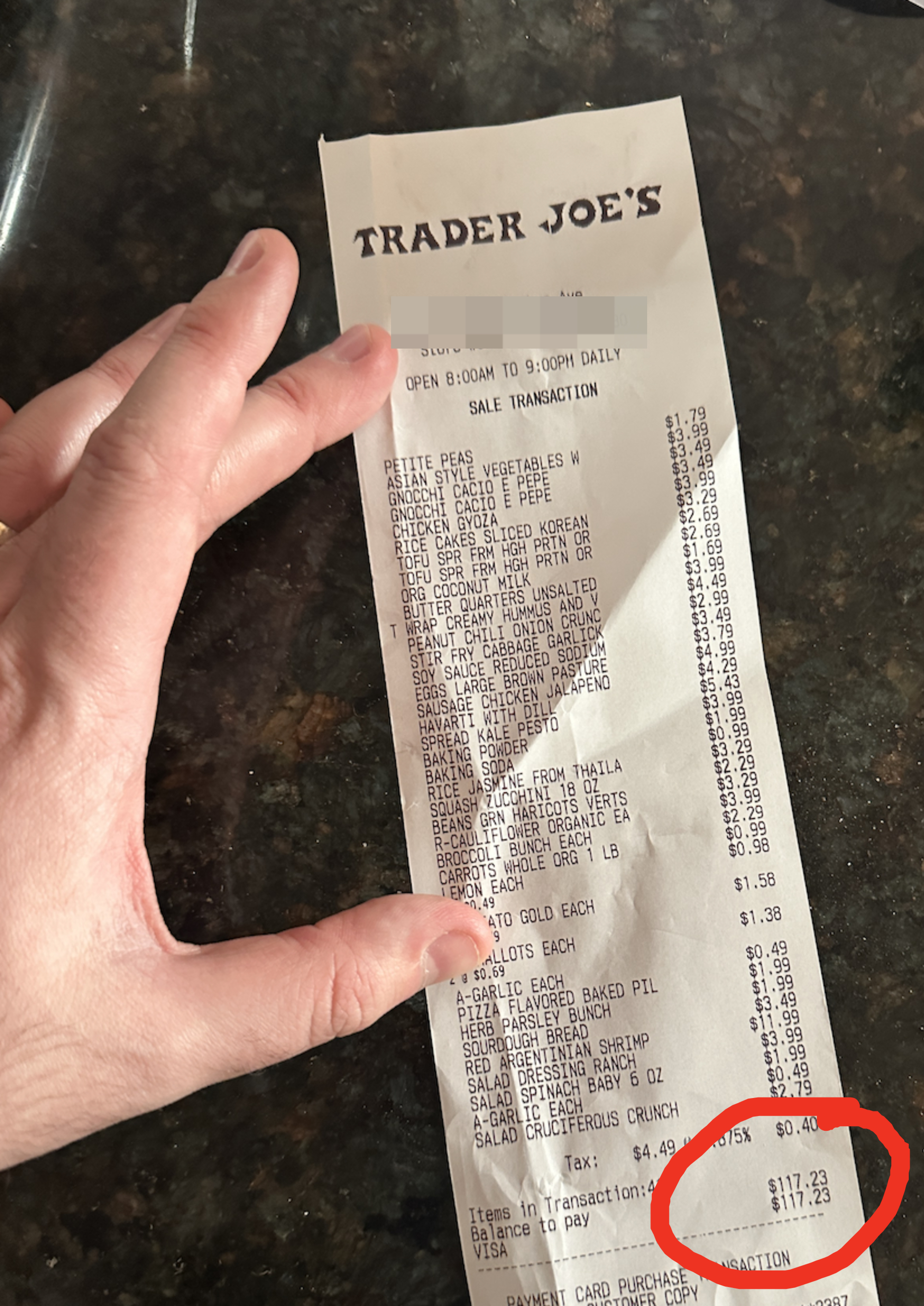 Hand holding a Trader Joe&#x27;s receipt listing various grocery items and their prices, with a total of $117.43 at the bottom