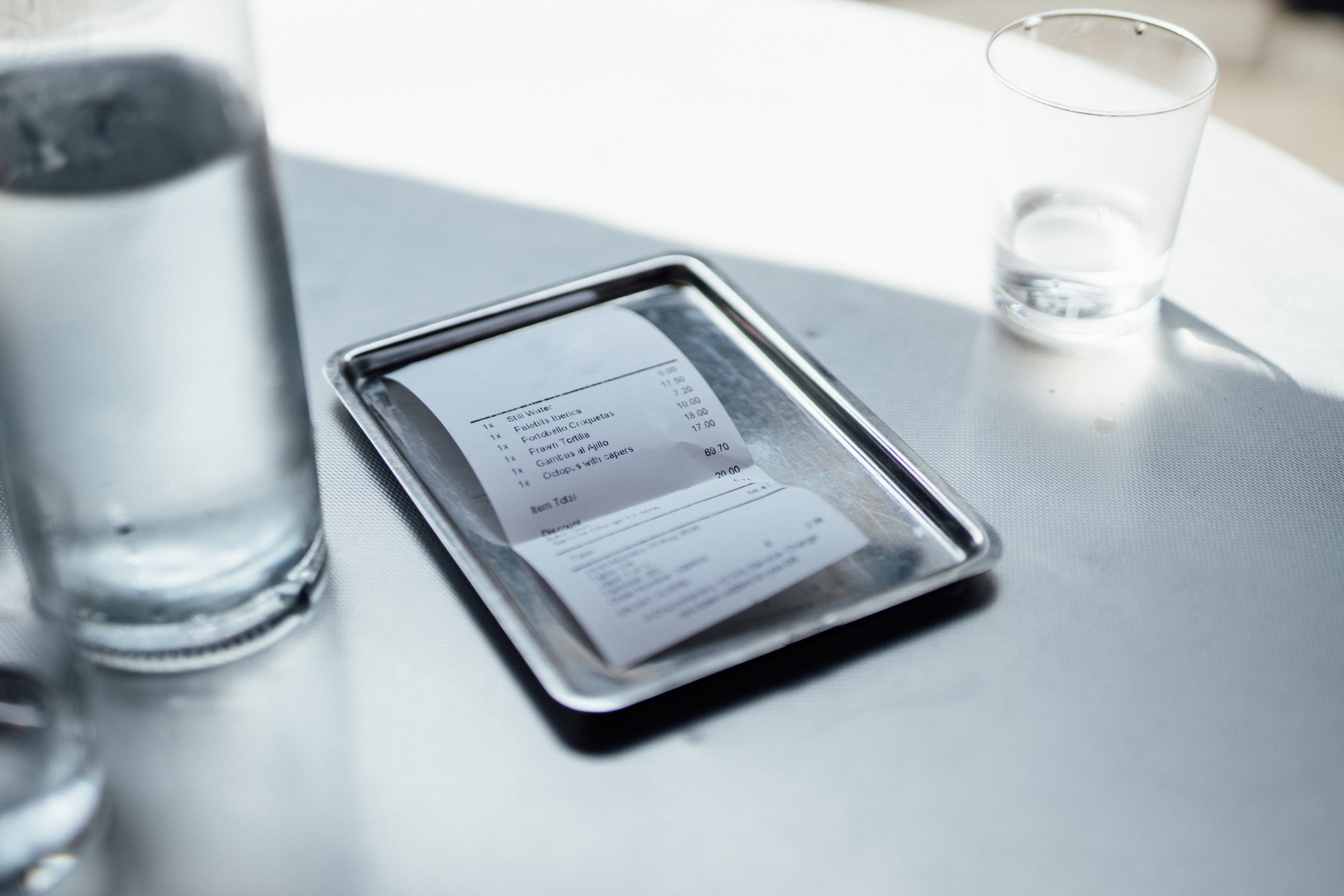 a restaurant check on a table beside a glass of water
