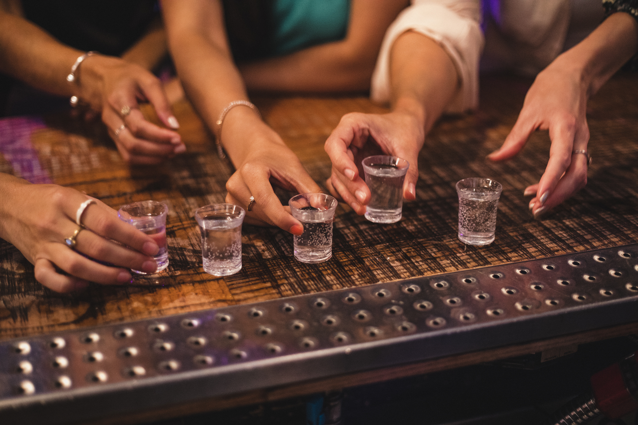 Several hands reaching for shot glasses on a bar counter