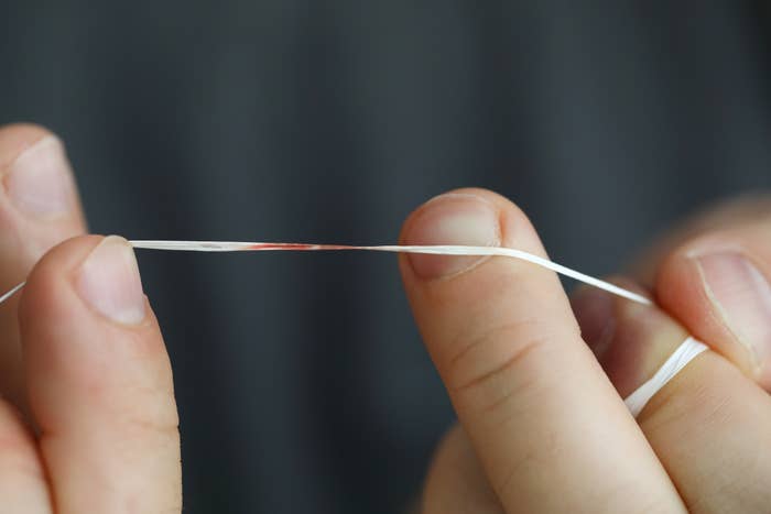 Close-up of a person&#x27;s hands holding a strand of dental floss with a small blood spot