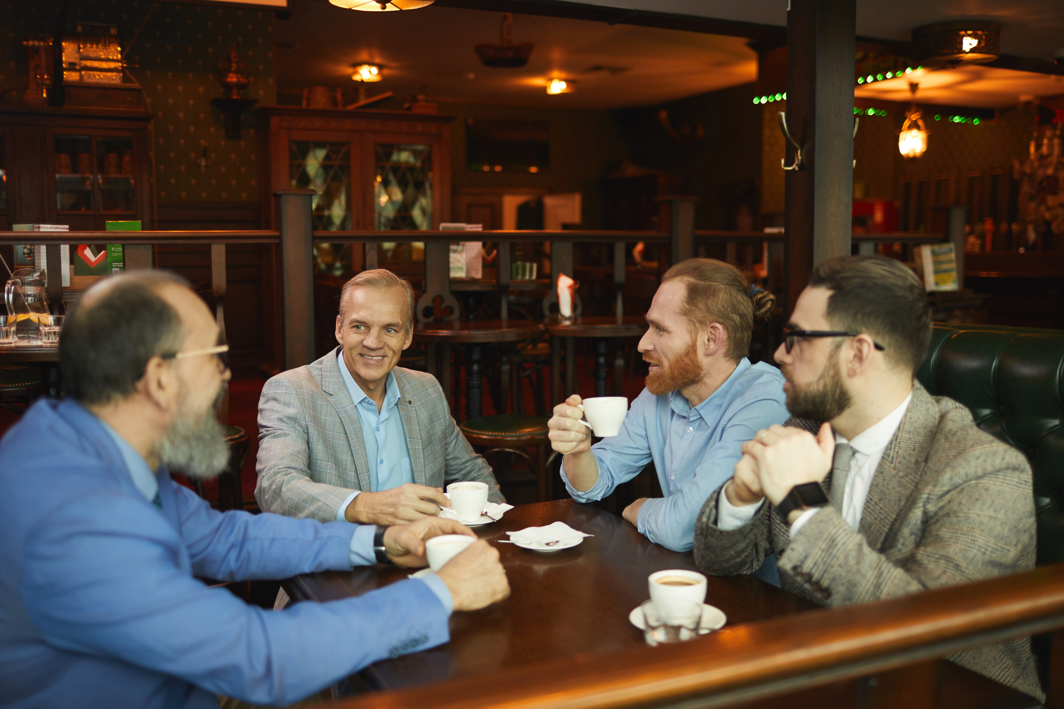 Four men engaging in conversation while holding cups at a pub table
