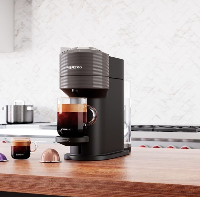 An espresso machine on a kitchen counter with a cup of coffee and capsules beside it