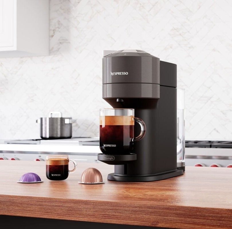 An espresso machine on a kitchen counter with a cup of coffee and capsules beside it