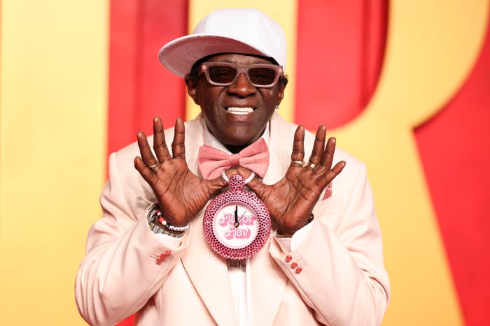 Man in a white hat and suit with a large pink bow tie and novelty glasses, posing playfully