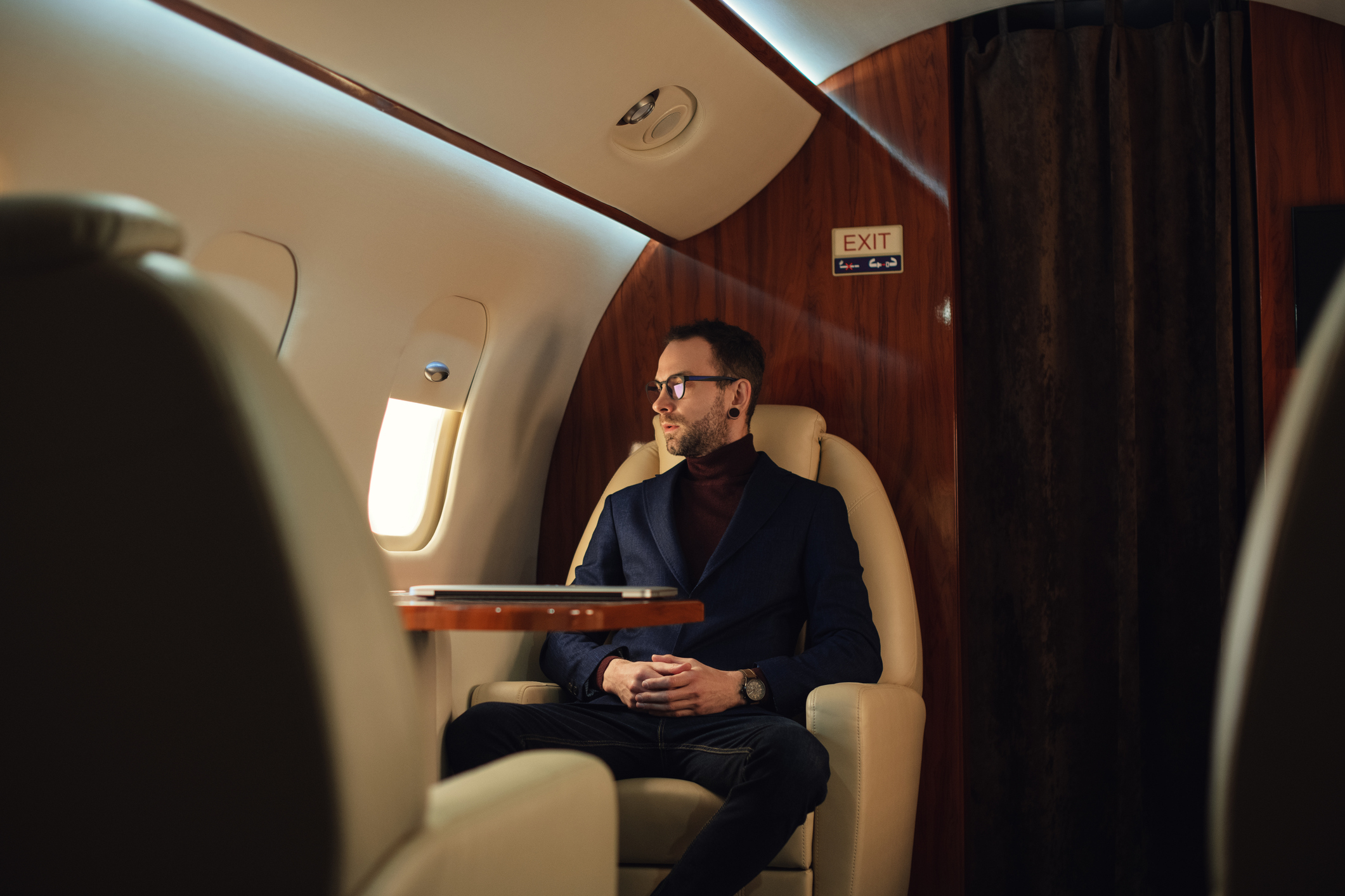 Man in business casual attire sitting in a private jet cabin, contemplating, exemplifying luxurious work travel