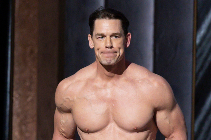 Man with muscular build in a non-descript location, expression focused