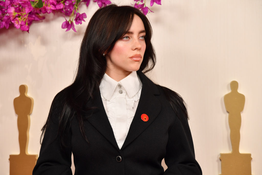 Billie Eilish at an event wearing a black suit with a white shirt and a red floral accessory