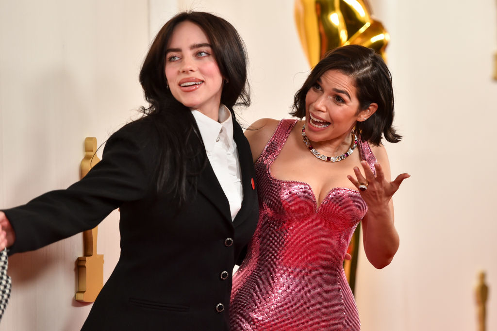 Billie Eilish in a black suit, next to Salma Hayek in a sparkling dress at an event