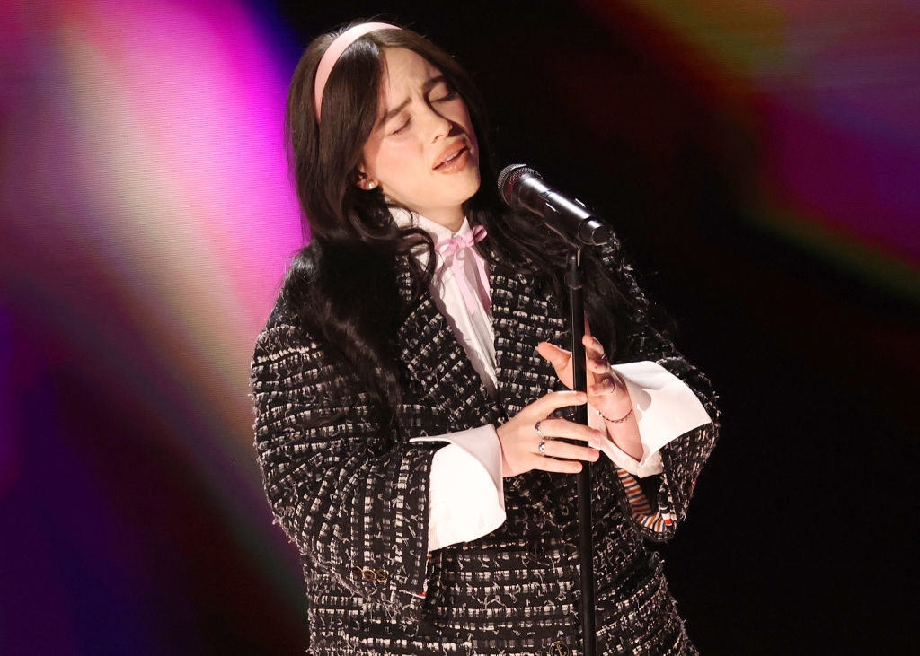 Billie Eilish performing on stage in a textured black suit with a bow tie