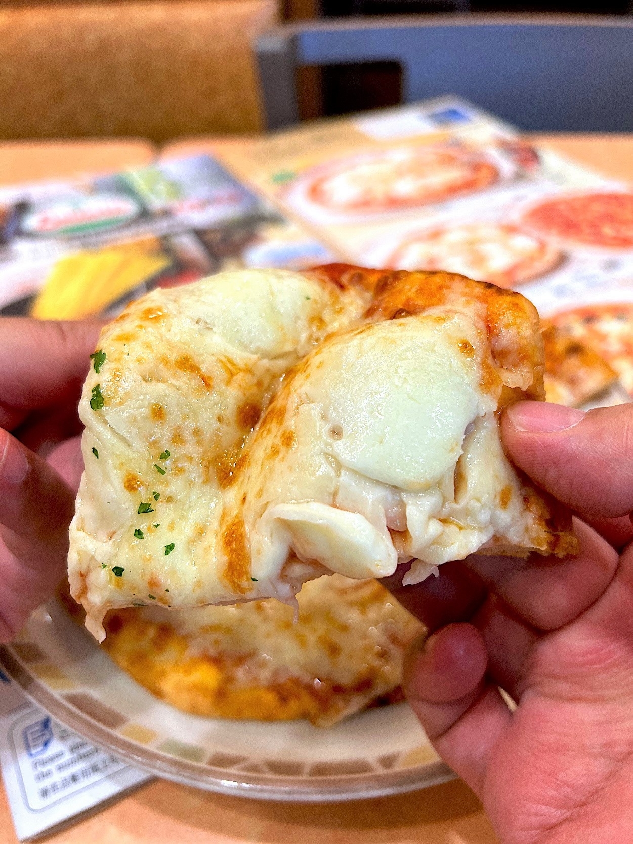 Person holding a slice of cheese pizza with visible stretchy cheese