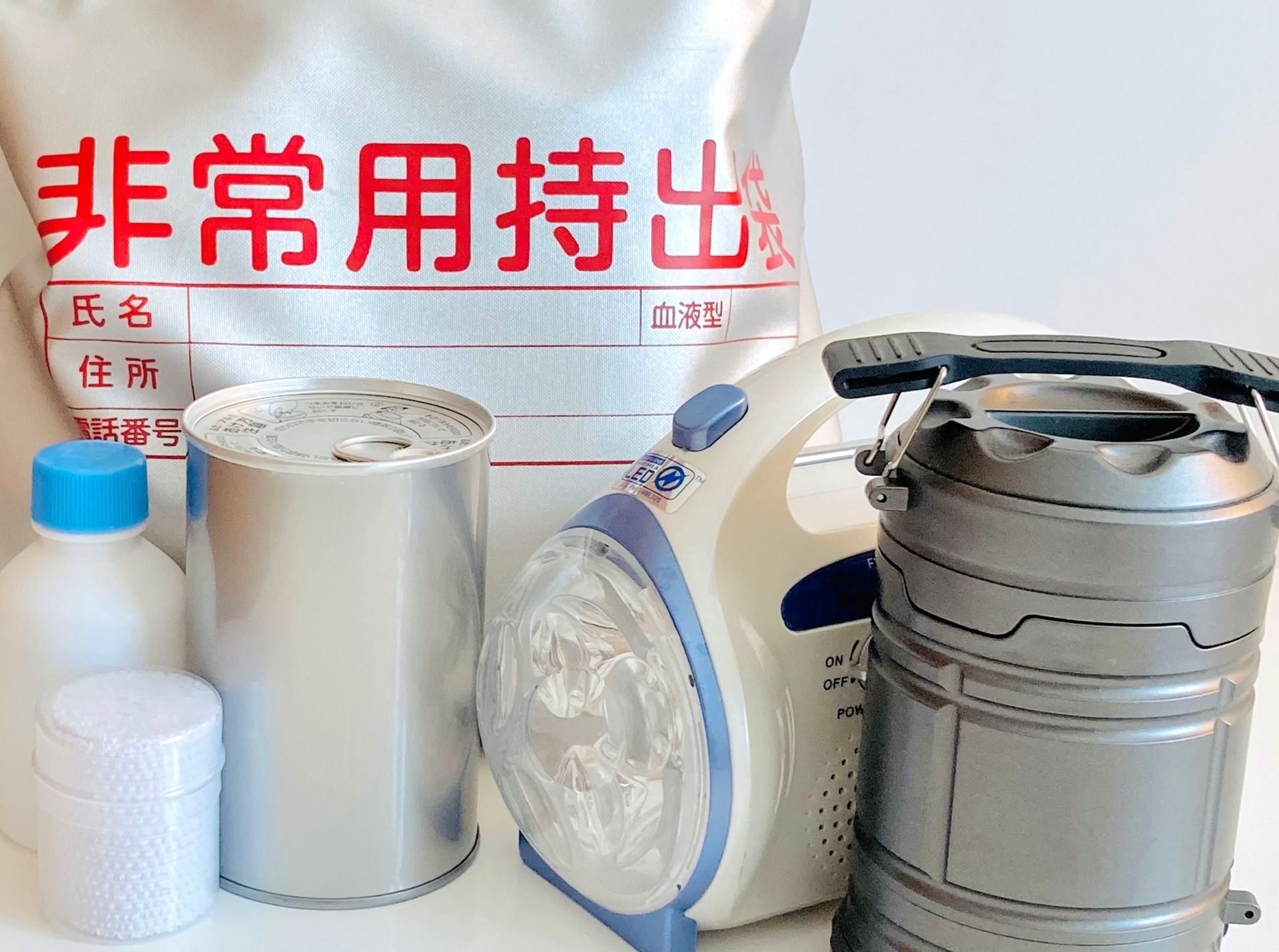 非常用持ち出し袋と蓄電式ランタン、水、食料が配置された防災グッズの写真です。