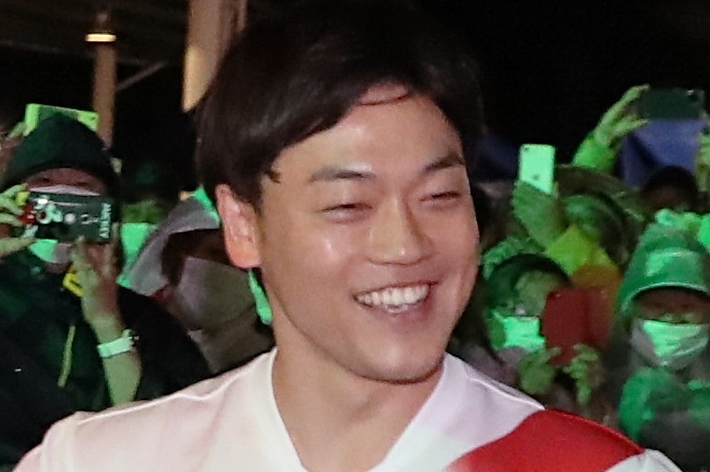 笑顔の男性が白いシャツを着ていて、背景には人々がいます。