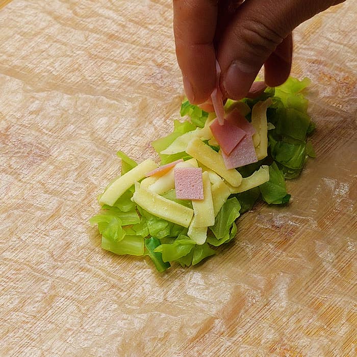手がサラダの具材をまな板の上で組み合わせている。