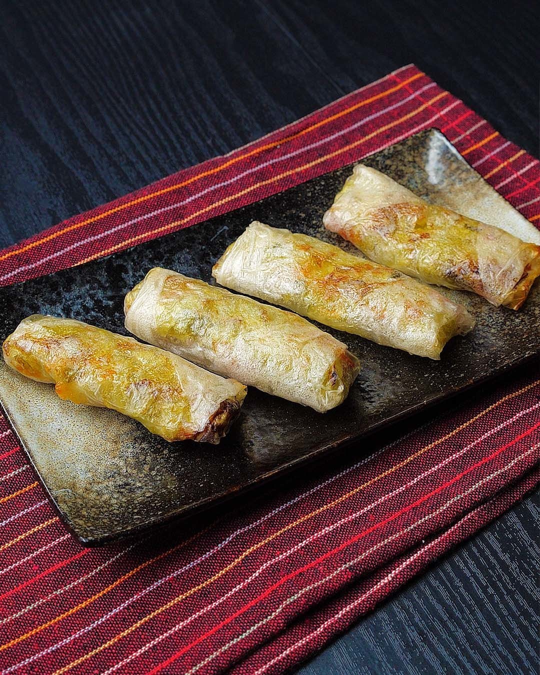 黒い背景の上にある皿の上に並べられた春巻き４つ。