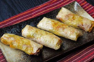 黒い背景の上にある皿の上に並べられた春巻き4つ。