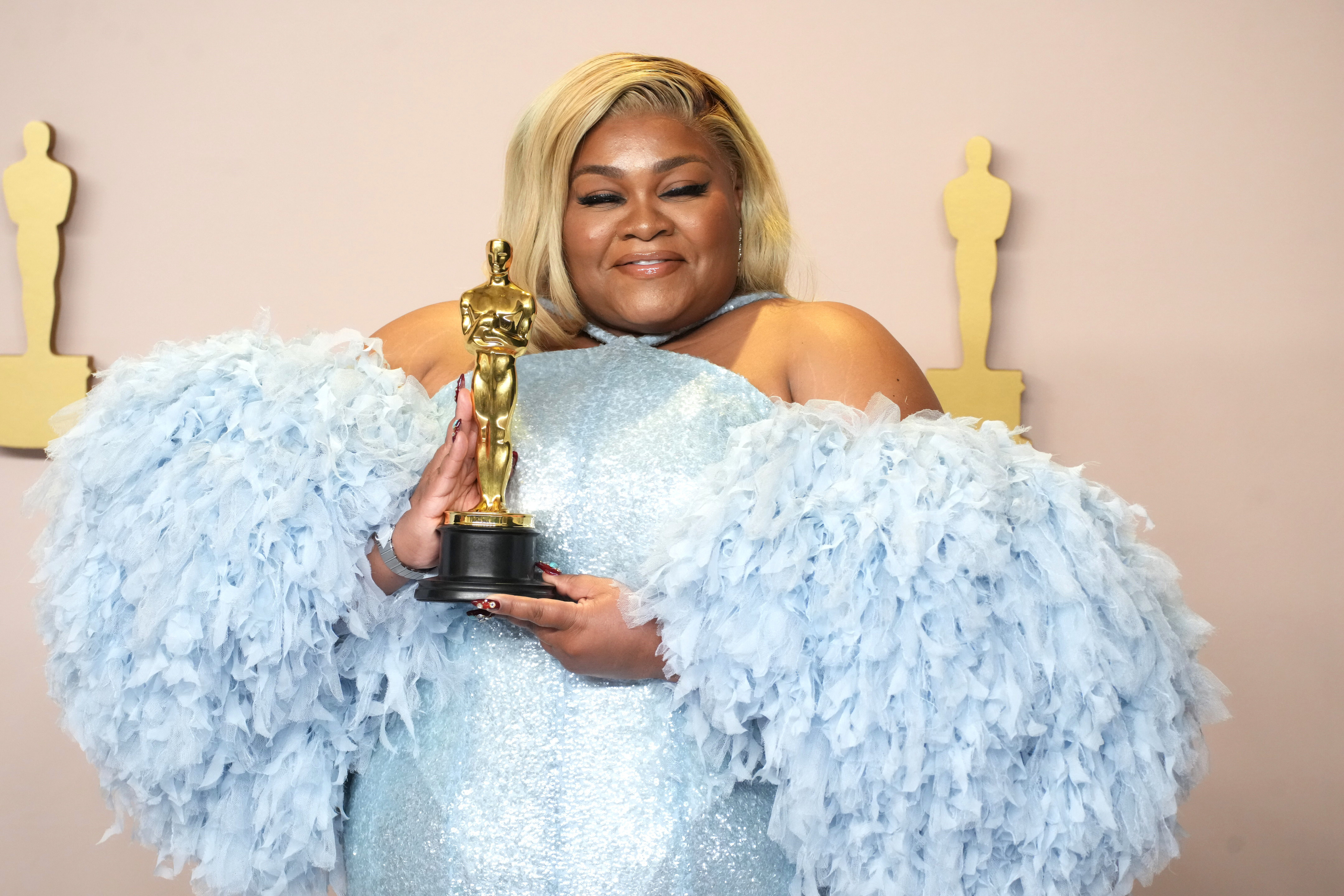 Da&#x27;Vine posing with her Oscar, wearing a sparkling dress with feathered sleeves