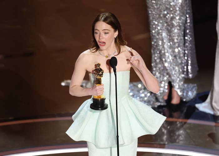 Actress giving an acceptance speech at an awards ceremony, holding a trophy, dressed in a stylish gown