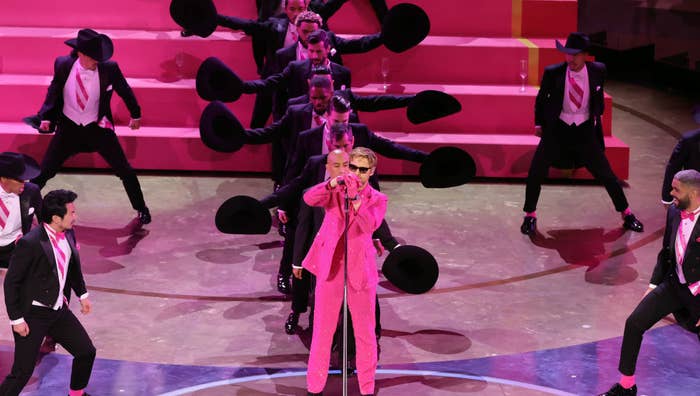 Performer in pink suit with dancers in black and pink on stage