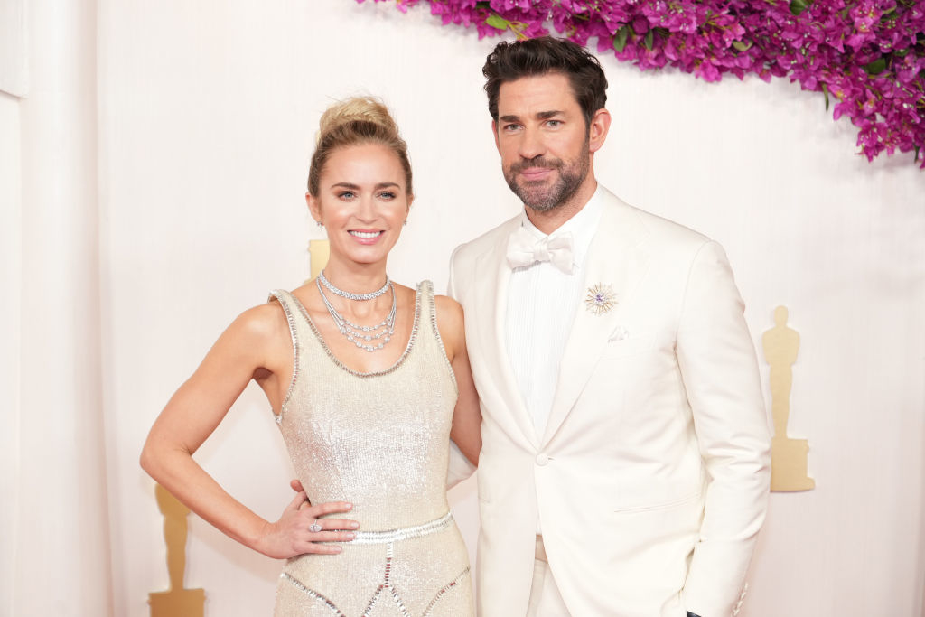 Emily Blunt in a glittering gown with layered necklaces and John Krasinski in a white tuxedo with a bow tie