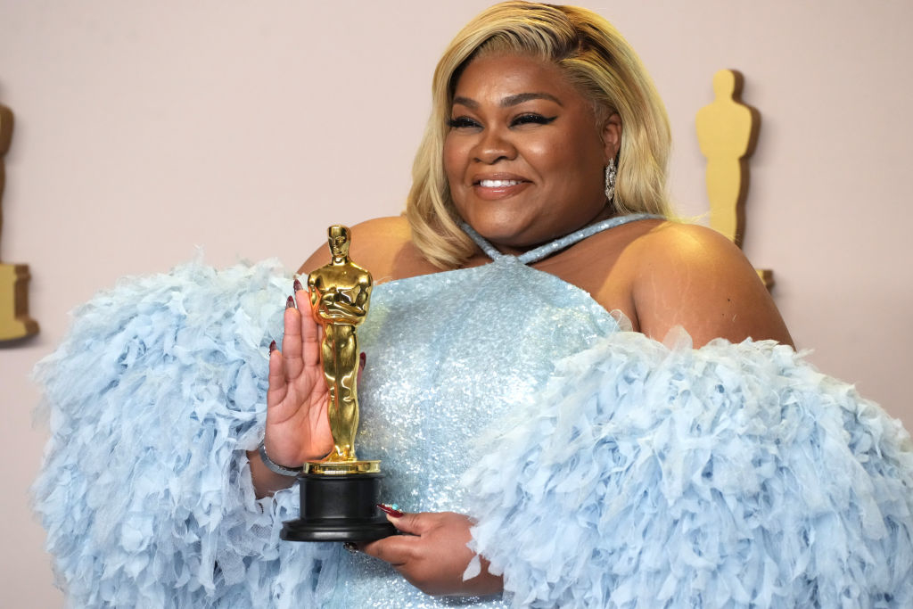 Da&#x27;Vine smiling, holding an Oscar award, wearing a sparkling dress with feathery details