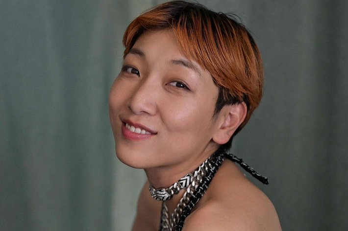 写真には笑顔の女性が写っており、彼女はメタリックなドレスを着用しています。