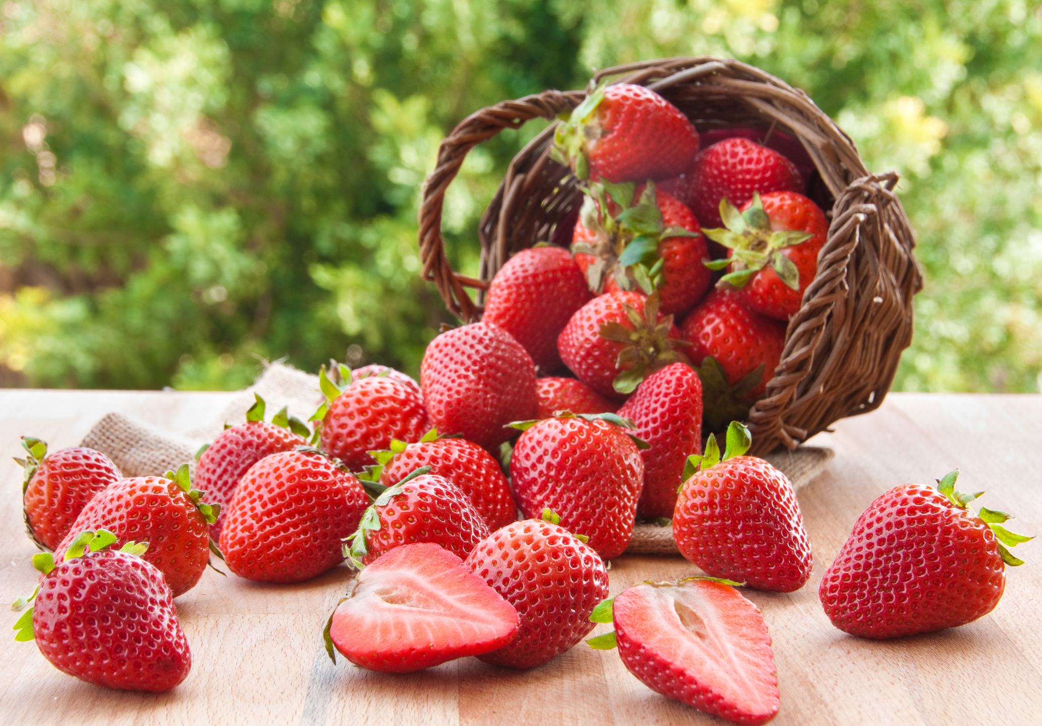 Fresh strawberries spilling from a basket onto a wooden surface, indicating agricultural produce business